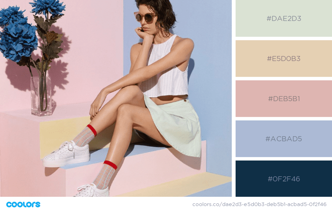 Mulher sentada em uma escada vestindo uma saia verde pastel, uma blusa branca, óculos de sol, meia cano médio e tênis brancos