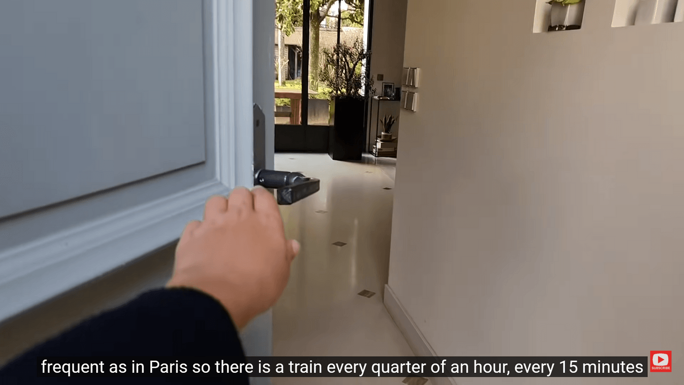 Hand opening door, subtitles read 'frequent as in Paris so there is a train every quarter of an hour, every 15 minutes.