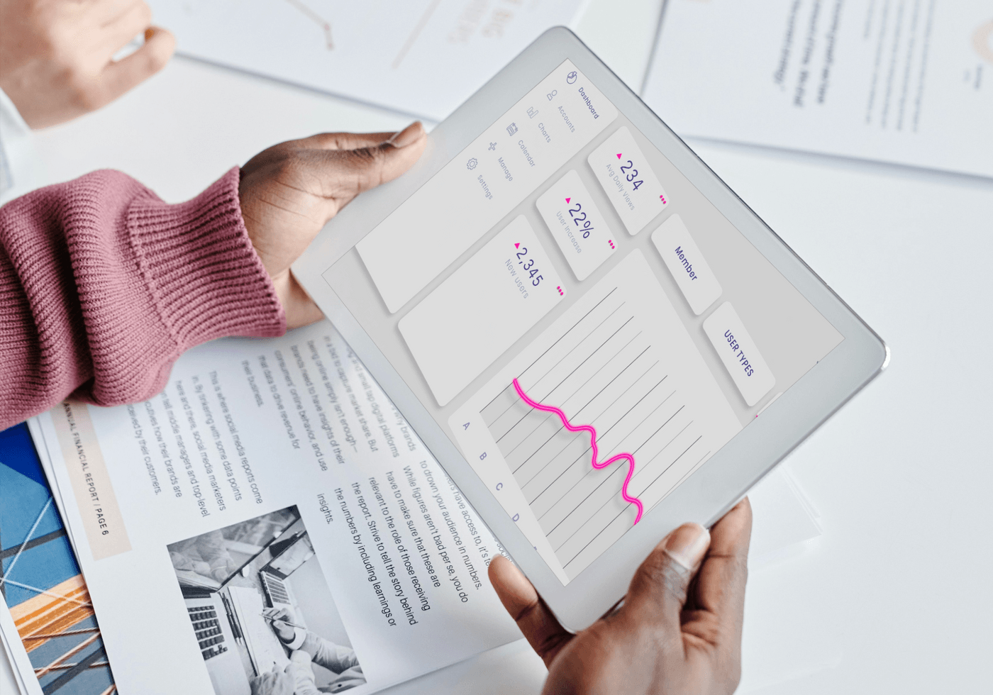 Person holding tablet showing analytics dashboard with graphs, user stats, and report on table