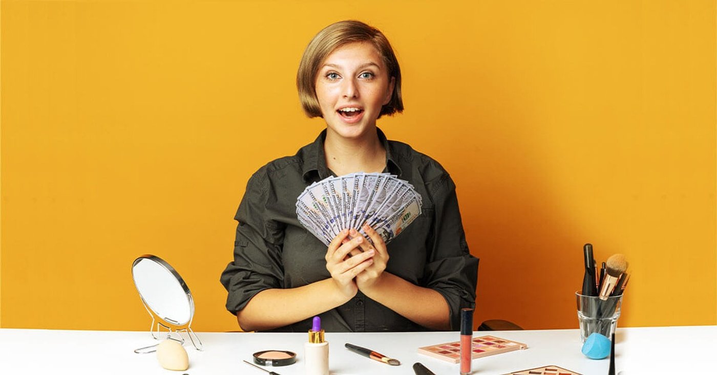 woman holding a fan of cash, sitting at a table with makeup tools