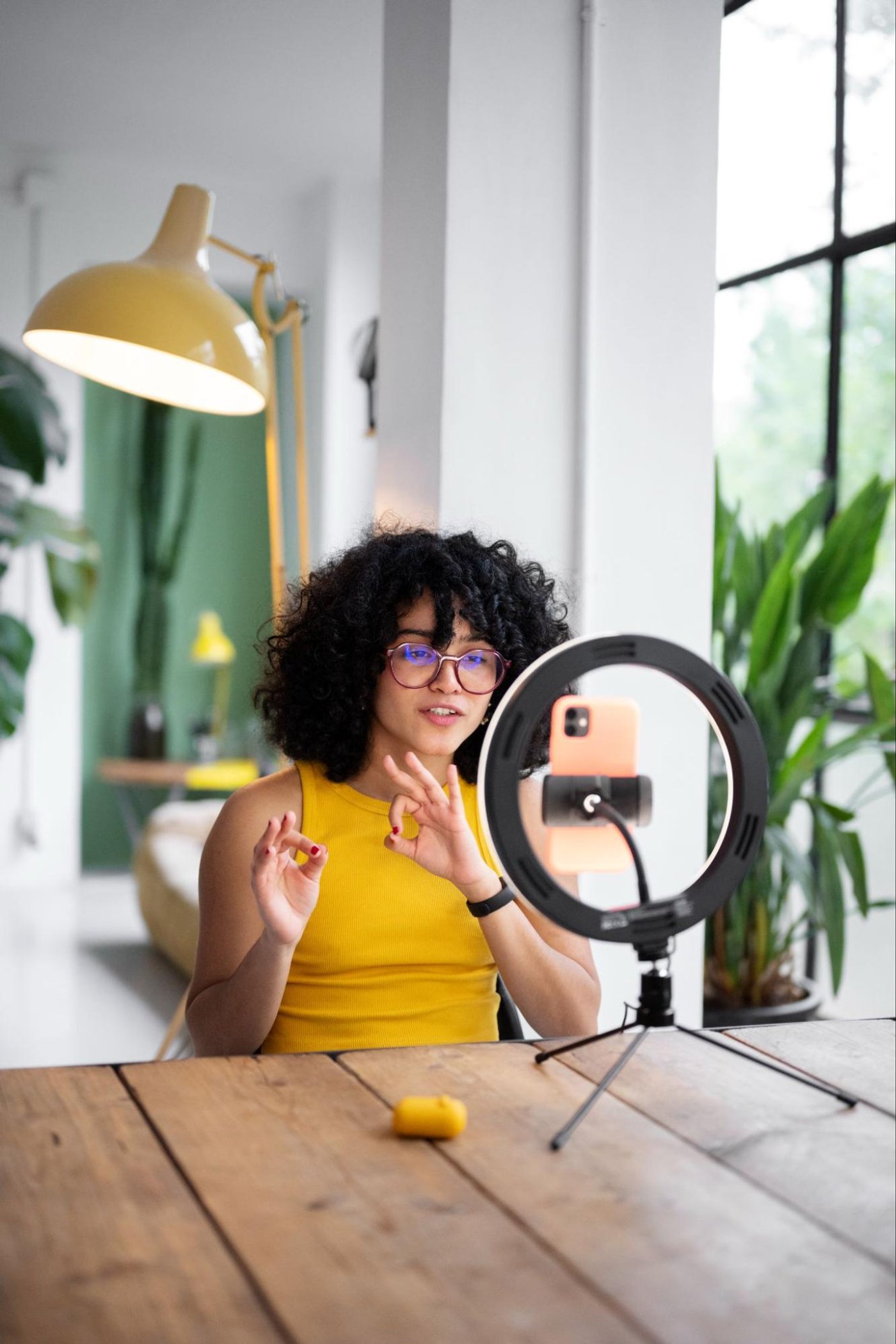woman recording video using smartphone on ring light, gesturing with hands at desk